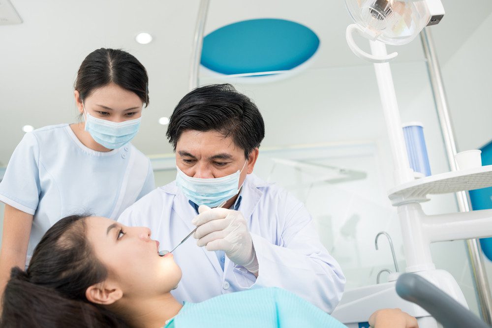 Mature dentist examining a patient sharing experience with his young intern
