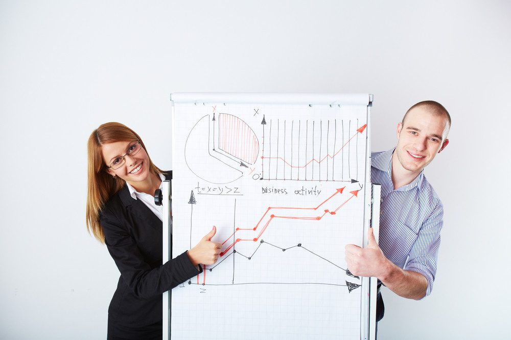 Successful business partners standing by whiteboard with graph of market analysis - OrthoSynetics