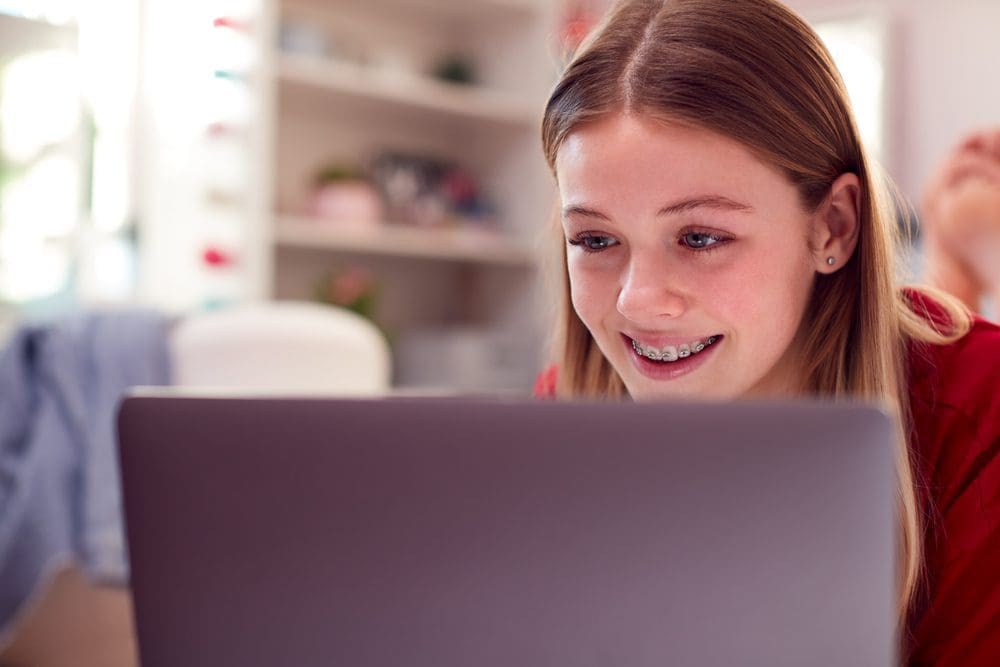 Teenage Girl with braces Wearing Pyjamas Using Laptop Lying On Bed In Bedroom