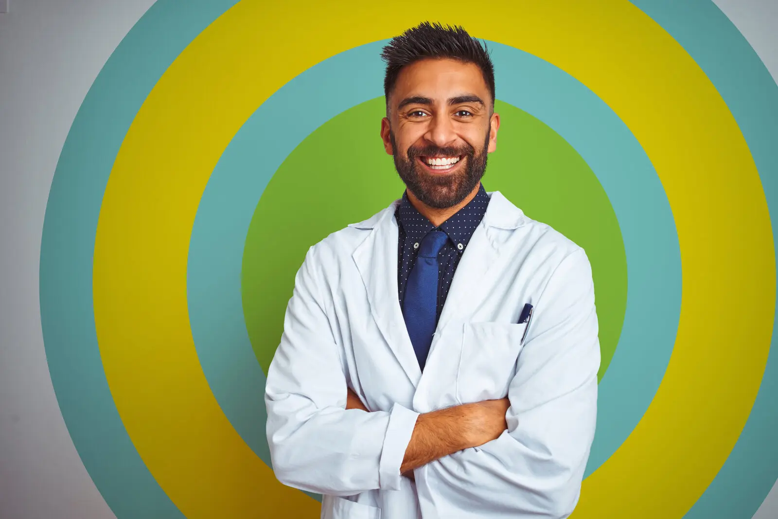 Young indian doctor man standing over isolated white background happy face smiling with crossed arms looking at the camera. Positive person.